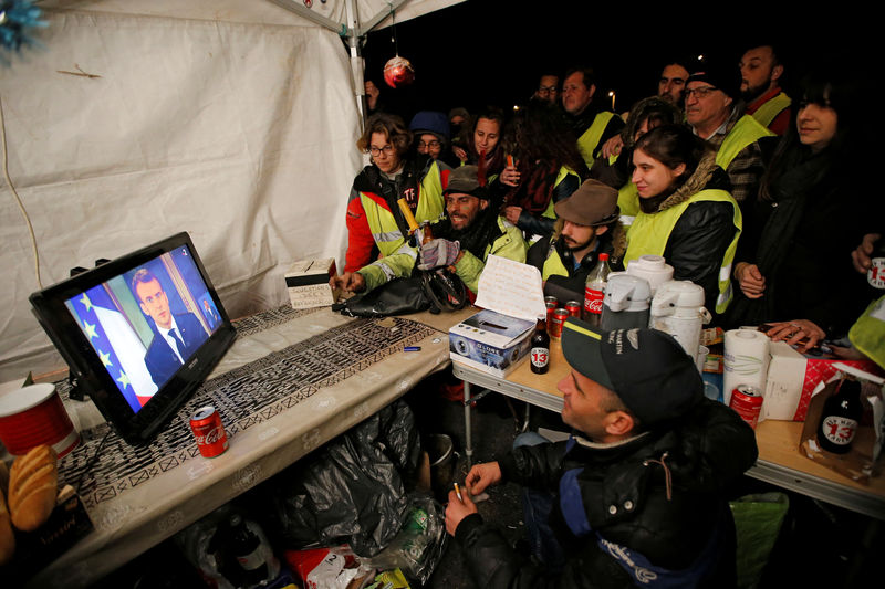 © Reuters. Protesters wearing yellow vests watch French President Emmanuel Macron on a TV screen at the motorway toll booth in La Ciotat