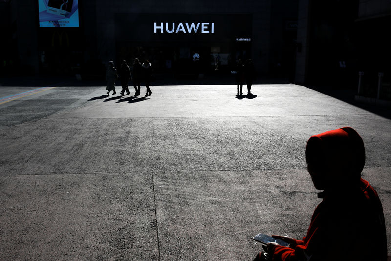 © Reuters. A man uses his phone as he sits in front of a Huawei shop in Beijing