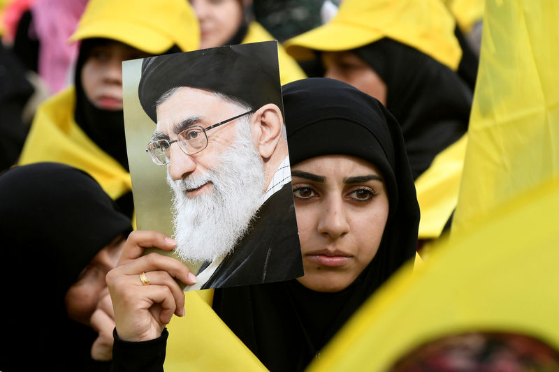 © Reuters. FILE PHOTO: A woman carries a picture of Iran's Supreme Leade Khamenei as she watches Lebanon's Hezbollah leader Nasrallah appear on a screen during a live broadcast to speak to his supporters at an event marking Resistance and Liberation Day in the Bekaa