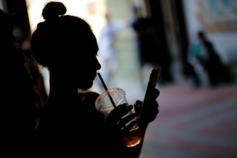 © Reuters. FILE PHOTO - A woman holds a drink while using her mobile phone on a hot summer day in Central Park, Manhattan, New York