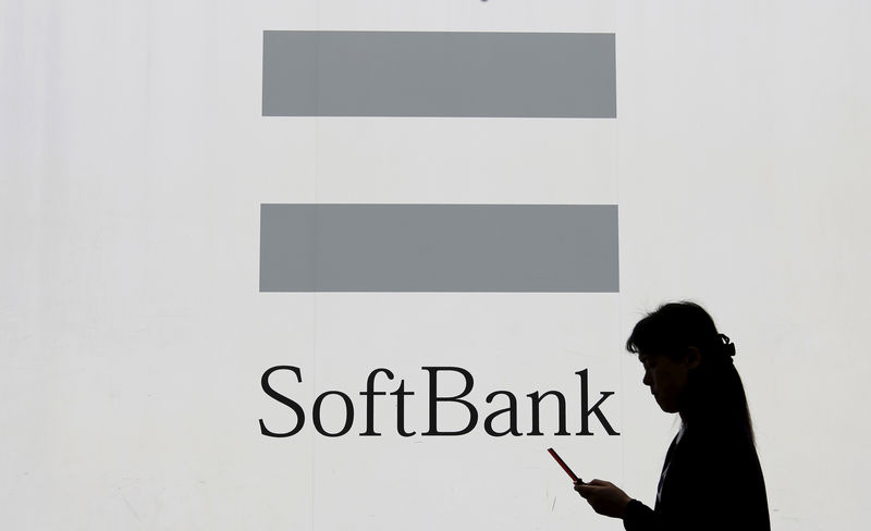 © Reuters. FILE PHOTO - A woman using a mobile phone walks past the logo of SoftBank Corp in Tokyo