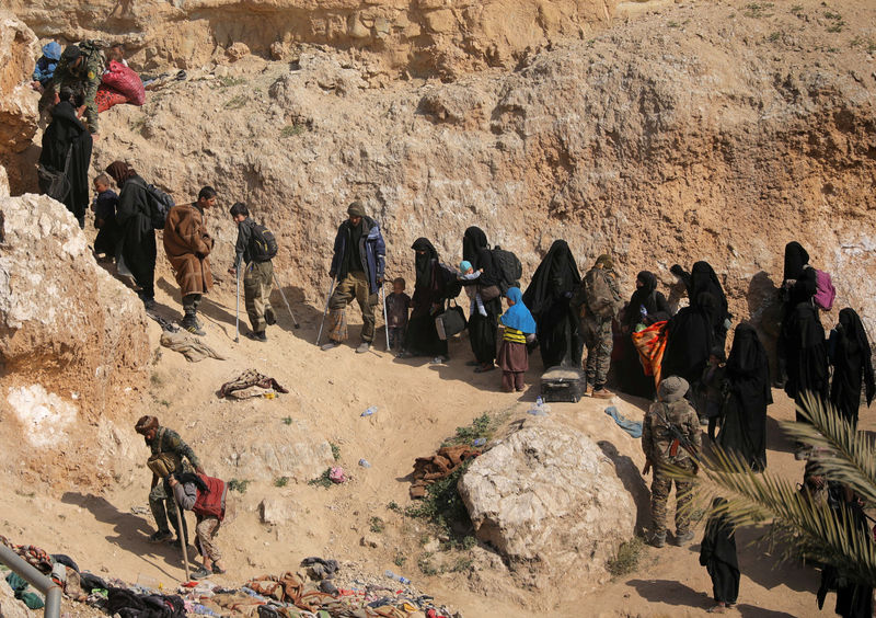 © Reuters. Combatentes do Estado Islâmico e familiares caminham para se render no vilarejo de Baghouz