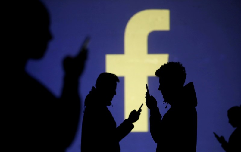 © Reuters. En la imagen de archivo, siluetas de personas entre un logo de Facebook