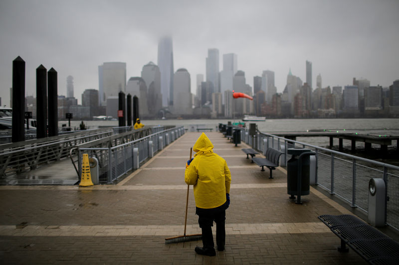 © Reuters. Un trabajador del ferry limpia el camino para los viajeros durante las nevadas ligeras, mientras que el horizonte de Nueva York y el One World Trade Center se ven desde Exchange Place