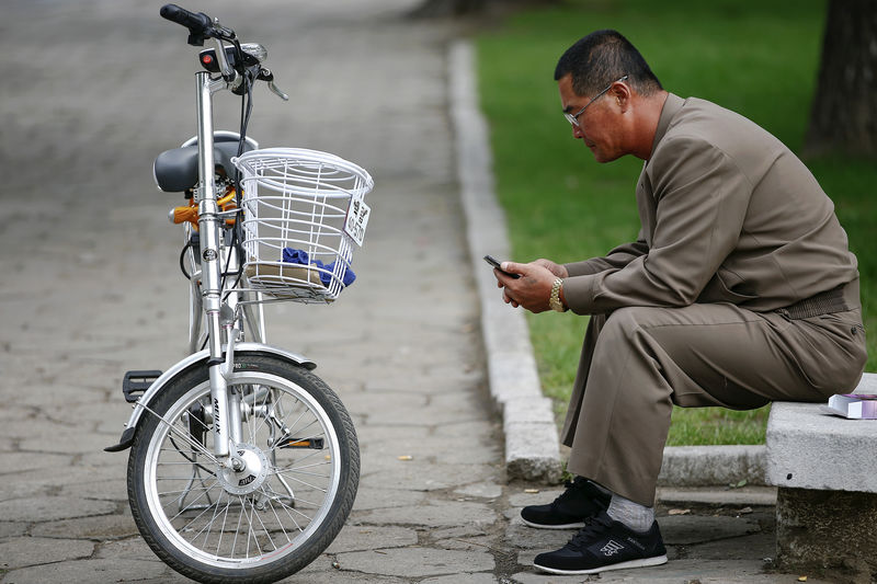 © Reuters. FILE PHOTO : A man uses his mobile phone next to an electric bicycle in downtown Pyongyang