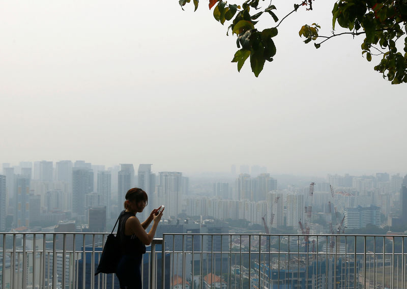 © Reuters. FILE PHOTO: A woman uses her phone on an observation deck as the skyline, shrouded by haze, is seen in Singapore