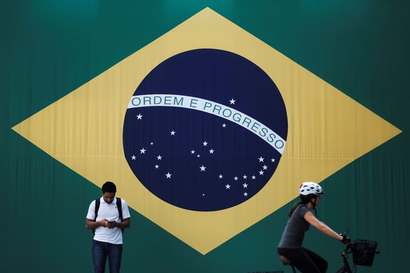 © Reuters. FILE PHOTO: A man checks his mobile phone as a woman riding a bike passes next to a big Brazilian flag in Sao Paulo