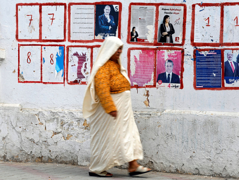 © Reuters. Woman walks past an election campaign poster of Tunisian media mogul Karoui in Tunis
