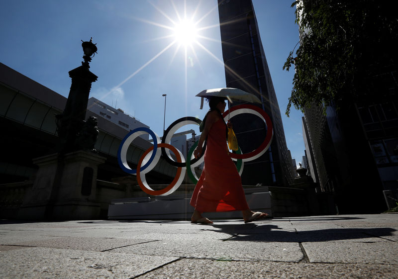 © Reuters. A woman holding a sunshade walks past Olympic rings displayed at Nihonbashi district in Tokyo