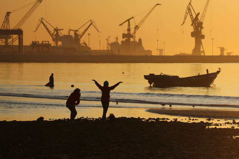 © Reuters. People enjoy the beach near a port during sunrise in Qinhuangdao