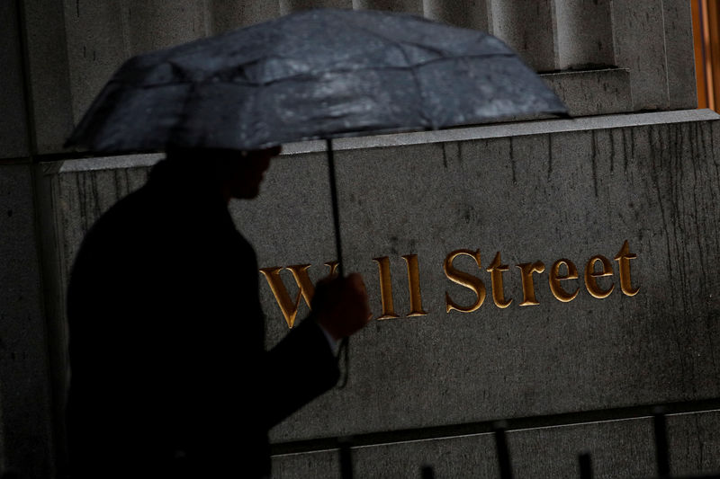 © Reuters. Мужчина под зонтом на Уолл-стрит около здания фондовой биржи в Нью-Йорке