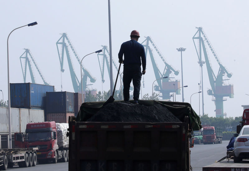 © Reuters. FILE PHOTO: A labourer loads coal in a truck next to containers outside a logistics center near Tianjin Port