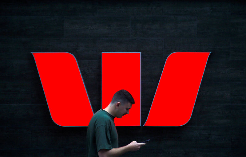 © Reuters. FILE PHOTO: A pedestrian looks at his phone as he walks past a logo for Australia's Westpac Banking Corp located outside a branch in central Sydney