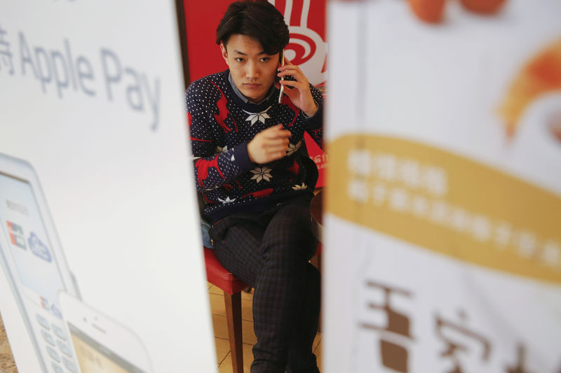 © Reuters. FILE PHOTO: A man speaks on the phone behind a banner advertising the Apple Pay service at a shopping centre in Beijing