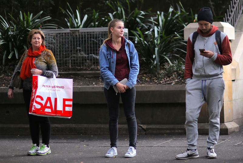 © Reuters. A woman carries her shopping bag containing purchased goods as she stands with other commuters at a bus stop in central Sydney