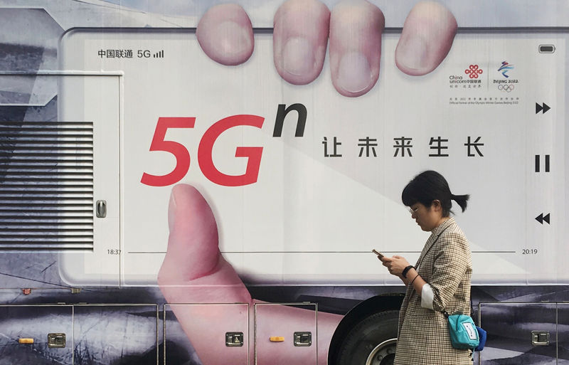 © Reuters. Una mujer usa su teléfono móvil mientras pasa junto a un vehículo con un anuncio de China Unicom 5G en Pekín.