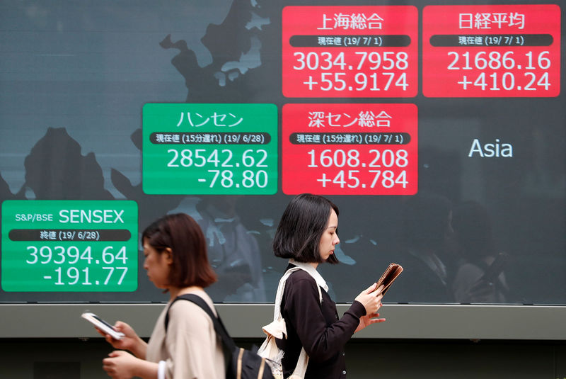 © Reuters. Passerbys walk past an electric screen showing Asian markets indices outside a brokerage in Tokyo