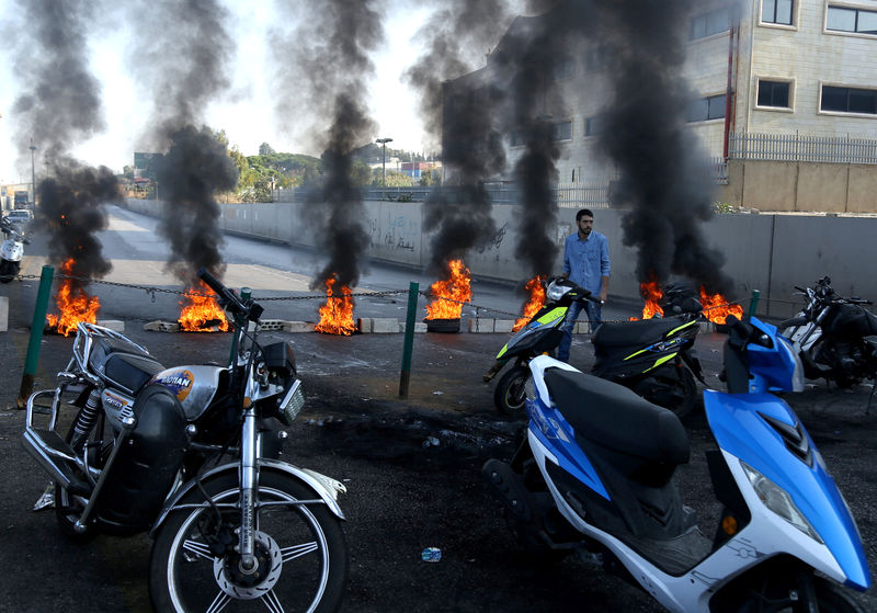 © Reuters. A demonstrator walks past a closed road by burning tires during ongoing anti-government protests, in Khaldeh
