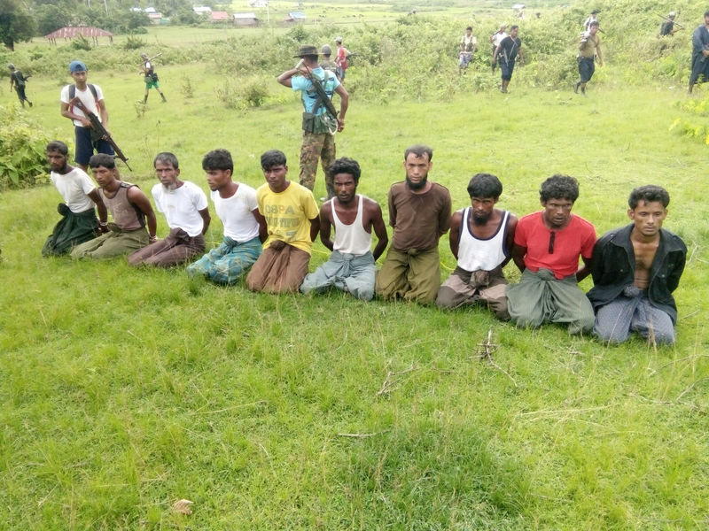 © Reuters. Ten Rohingya men with their hands bound kneel as members of the Myanmar security forces stand guard in Inn Din village