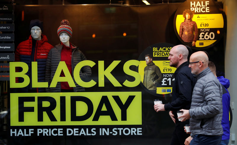 © Reuters. People walk past a sign advertising Black Friday offers in the window of a Blacks outdoor clothing store in Manchester, Britain