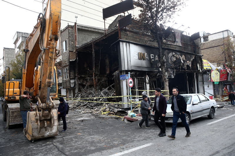 © Reuters. People walk near a burnt bank, after protests against increased fuel prices, in Tehran