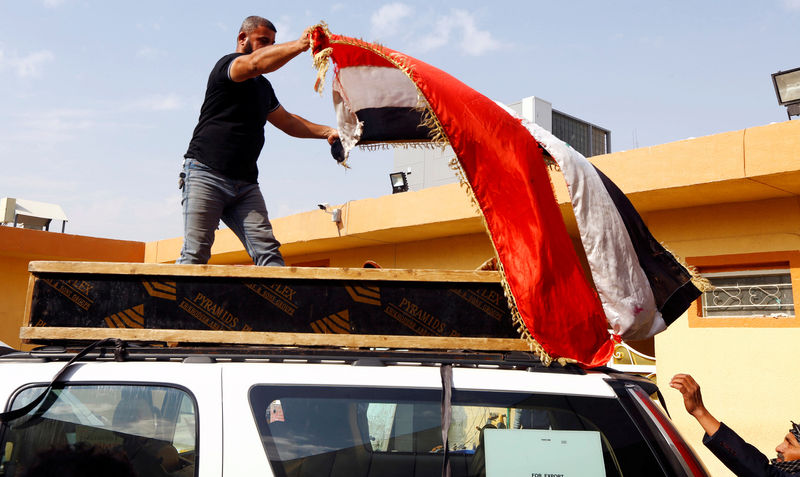 © Reuters. A man puts an Iraqi flag on the coffin of a demonstrator who was killed at anti-government protests in Nassiriya, during the funeral in Najaf