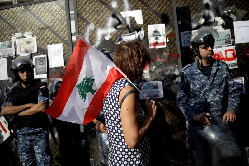 © Reuters. FILE PHOTO: A protester holds a Lebanese flag as she walks in front of police officers stand guarding the Lebanon Central Bank at a demonstration during ongoing anti-government protests in Beirut