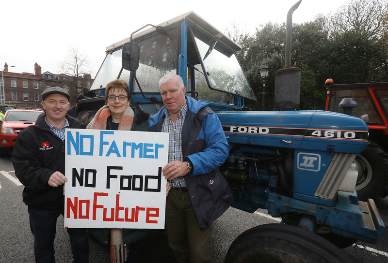 © Reuters. Protesting farmers Seamus McCaul, Mary Cooney and Frankie McCaul from Cavan hold a sign outside the Shelbourne Hotel, as they block St Stephen's Green with their tractors, in Dublin