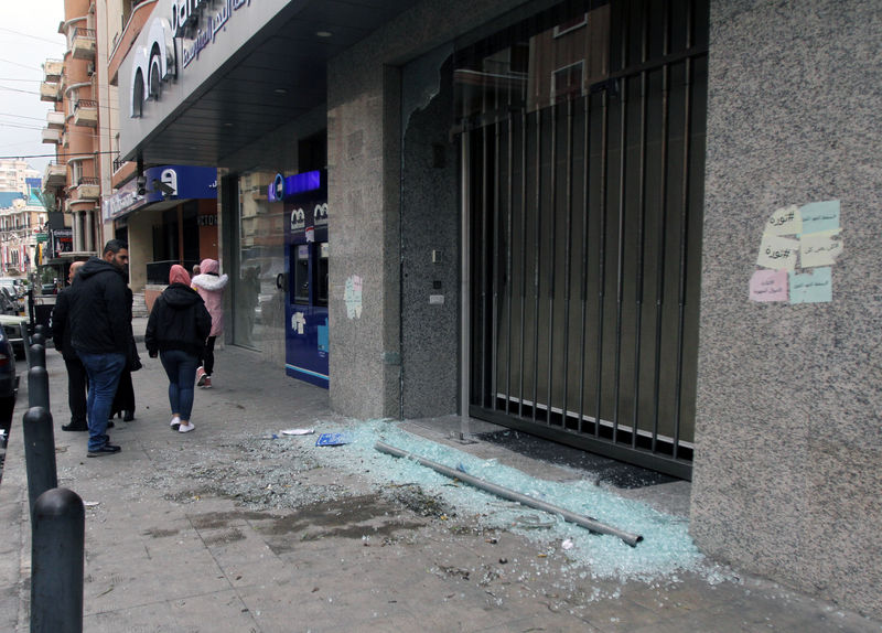 © Reuters. Men walk near broken glass from a damaged Bankmed branch in Tripoli