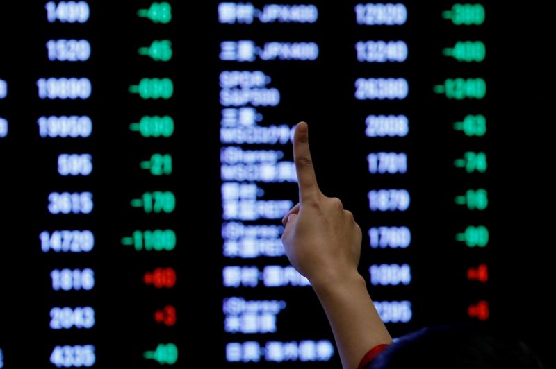 © Reuters. FILE PHOTO: A woman points to an electronic board showing stock prices as she poses in front of the board after the New Year opening ceremony at the Tokyo Stock Exchange (TSE), held to wish for the success of Japan's stock market, in Tokyo