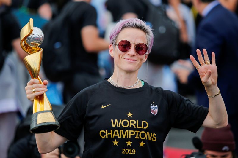 © Reuters. FILE PHOTO: Megan Rapinoe gestures the number 4 with her fingers as she holds the Trophy for the FIFA Women's World Cup while the U.S. team arrives at the Newark International Airport, in Newark