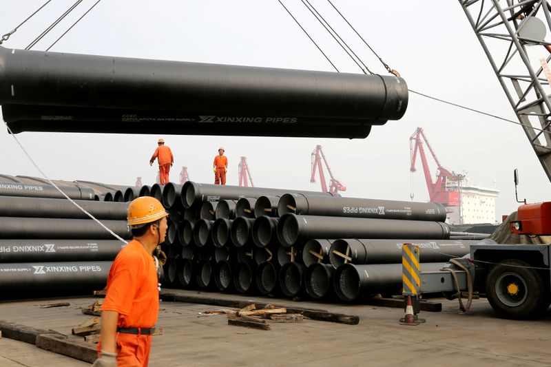 © Reuters. Workers direct a crane lifting ductile iron pipes for export at a port in Lianyungang, Jiangsu