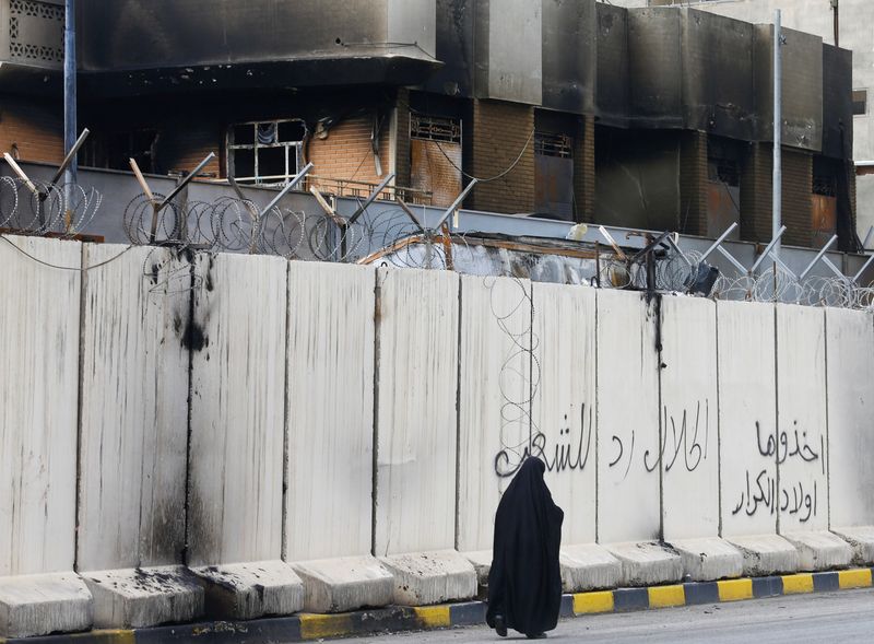 © Reuters. An Iraqi woman walks past the Iranian consulate after Iraqi demonstrators stormed and set fire to the building during ongoing anti-government protests in Najaf