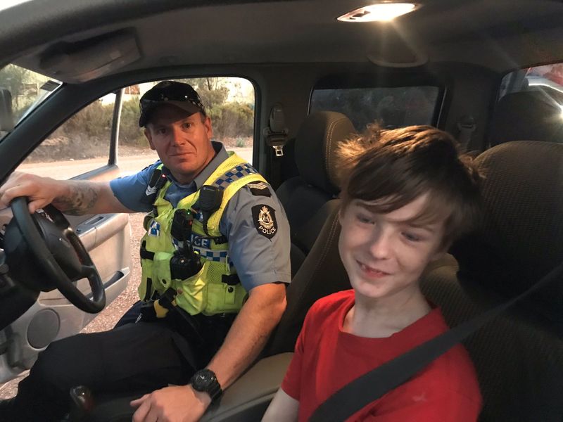 © Reuters. A 12 years old boy sits next to Dalwallinu Police officer S/C Smith after he drove across paddocks to escape the fire in Mogumber