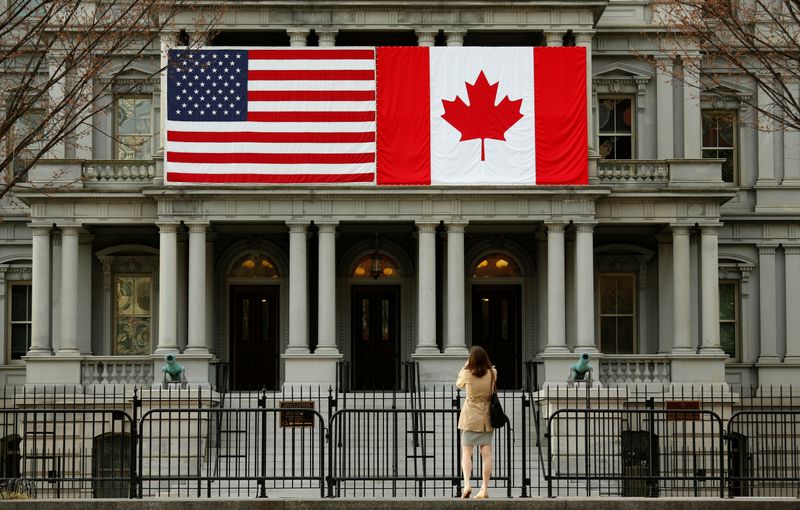 © Reuters. FILE PHOTO: A woman stops to take a photo of the U.S. and Canadian flags placed side-by-side on the Eisenhower Executive Office Building next to the White House in Washington