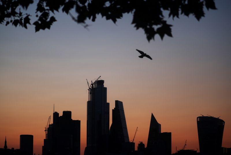 © Reuters. FILE PHOTO: A bird flies as the sun rises behind the city of London financial district in London