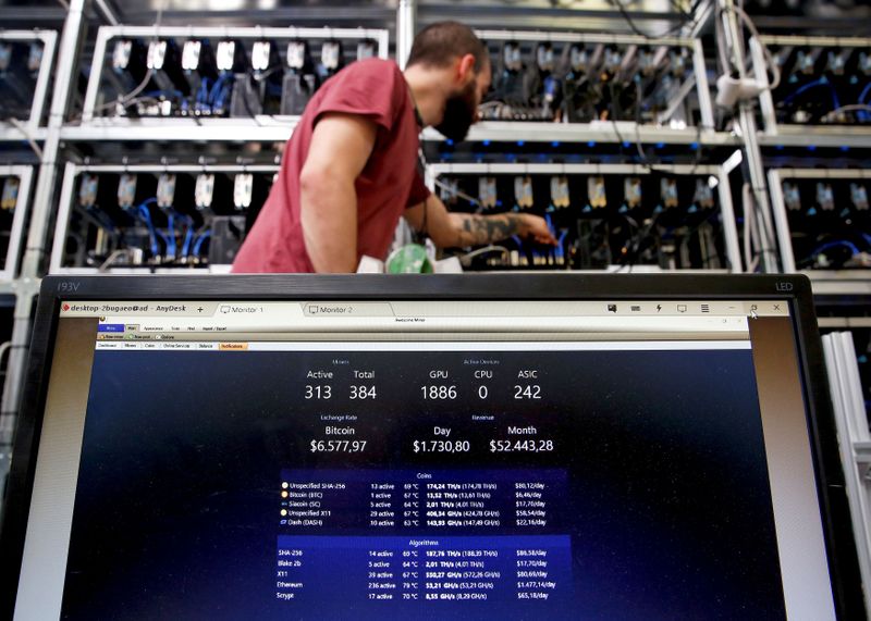 © Reuters. FILE PHOTO: An employee works on Bitcoin mining computer as a PC screen shows the fluctuations in Bitcoin exchange rates at Bitminer Factory in Florence