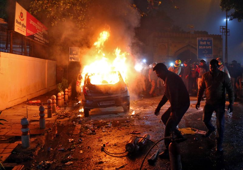 © Reuters. Men try to extinguish a burning car after demonstrators set it on fire during a protest against a new citizenship law, in New Delhi