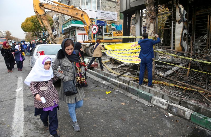© Reuters. FILE PHOTO: People walk near a burnt bank, after protests against increased fuel prices, in Tehran