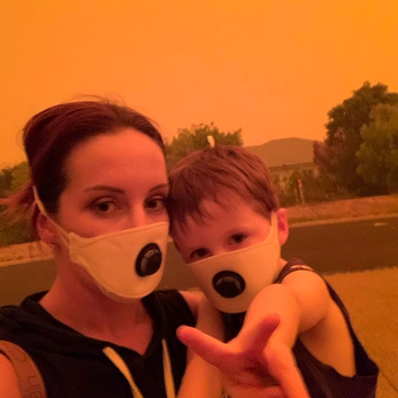 © Reuters. Amy Houghton and her son wearing masks stand under a sky tinted red as surrounding bushfires close in on the town of Mallacoota