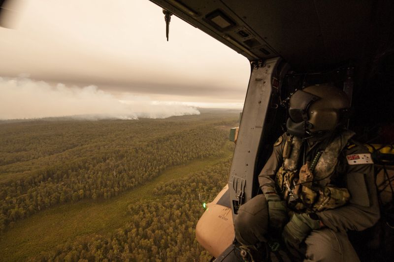 © Reuters. A Royal Australian Navy MRH-90 helicopter crew member, observes the fires on approach to Cann River in Gippsland