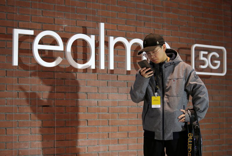 © Reuters. Man looks at mobile phone next to Realme logo during product launch event of X50 5G in Beijing