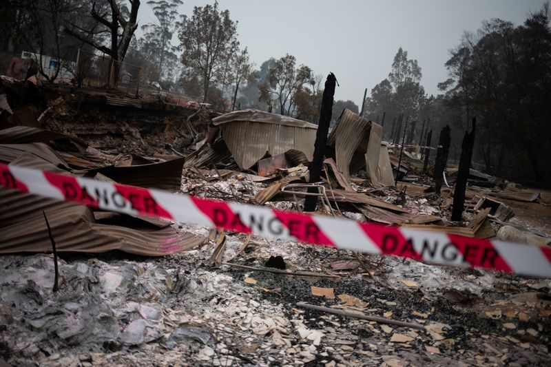 © Reuters. A cordon tape with the word "Danger" is seen in front of a burnt down shop in the village of Mogo