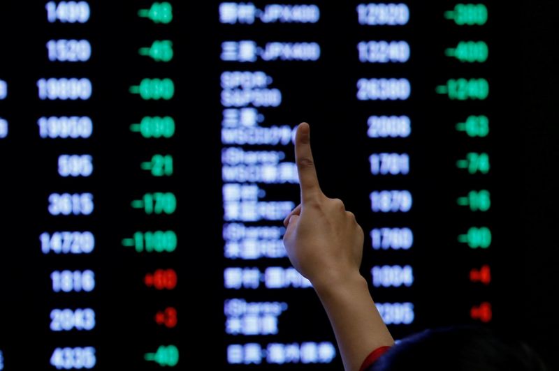 © Reuters. A woman points to an electronic board showing stock prices as she poses in front of the board after the New Year opening ceremony at the Tokyo Stock Exchange (TSE), held to wish for the success of Japan's stock market, in Tokyo
