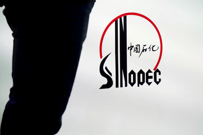 © Reuters. FILE PHOTO: Man stands next to a logo of Sinopec at an expo on rubber technology in Shanghai