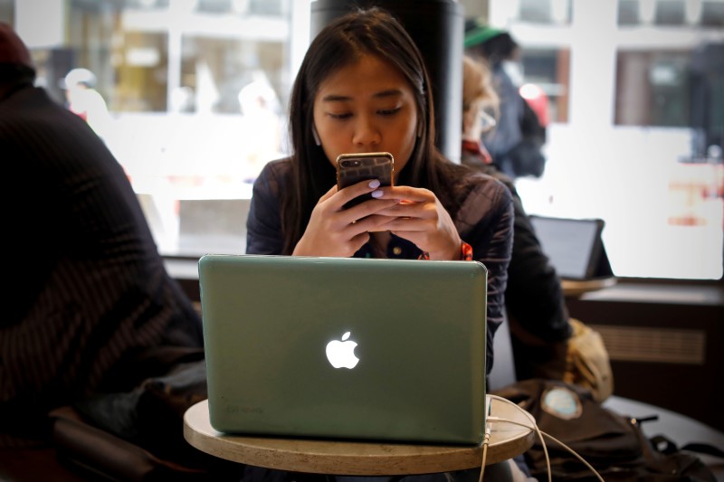 © Reuters. FILE PHOTO: A woman uses her Apple iPhone and laptop in a cafe in lower Manhattan in New York City
