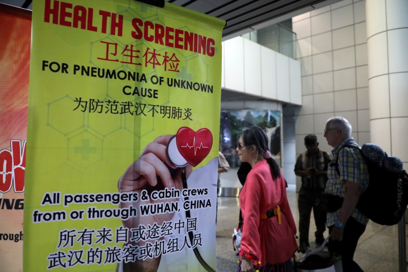 © Reuters. FILE PHOTO: Passengers pass a banner about Wuhan Pneumonia at a thermal screening point in the international arrival terminal of Kuala Lumpur International Airport in Sepang