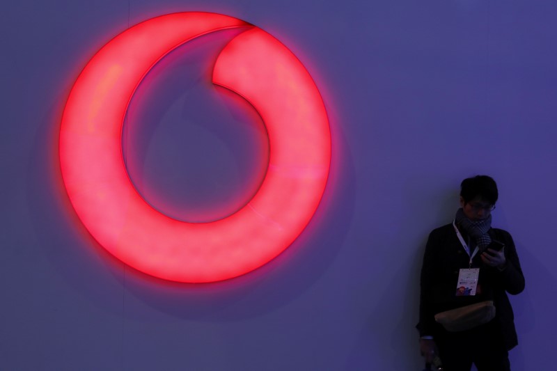 © Reuters. A man checks his mobile phone next to a Vodafone logo at the Mobile World Congress in Barcelona