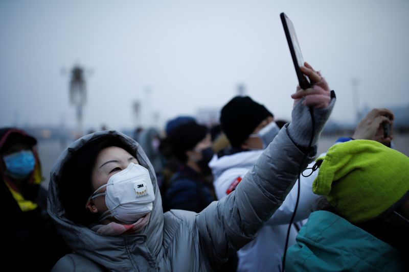 © Reuters. Una donna con una mascherina si fa un selfie con il telefono a Tiananmen Square, a Pechino