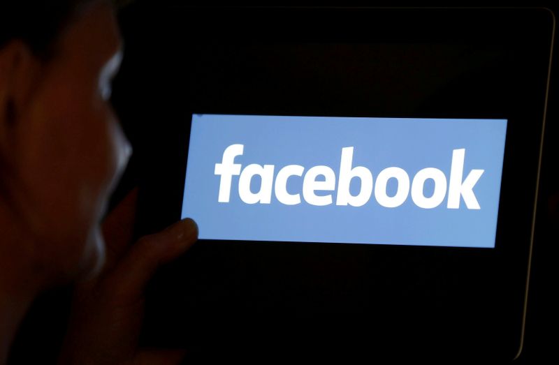 © Reuters. FILE PHOTO: A woman looks at the Facebook logo on a screen.
